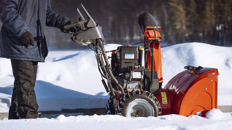 Man in black pants and a blue coat getting ready to use a snow blower