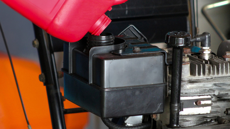 Pouring gas into a snow blower gas tank from a red gasoline container