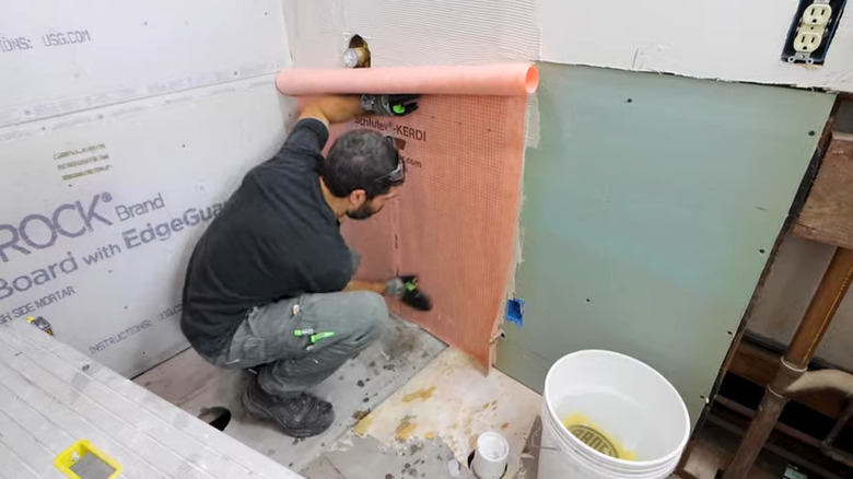 A worker applying waterproof membrane to shower walls