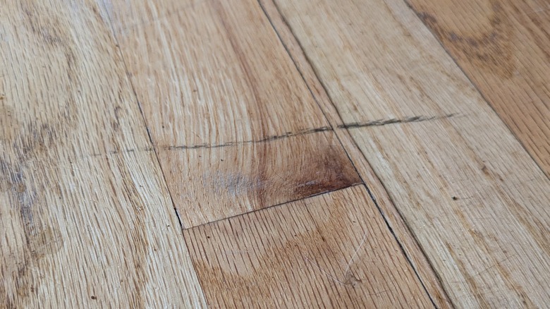 A black scuff mars a light hardwood floor.