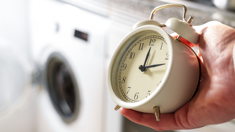 a person holding a clock in hand with a washing machine in the background