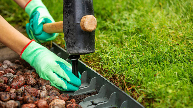 Person installing plastic landscape edging by driving a stake with a mallet