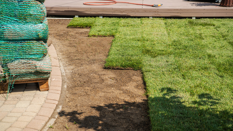 Yard being sodded with some bare soil and more rolls of sod in a pile