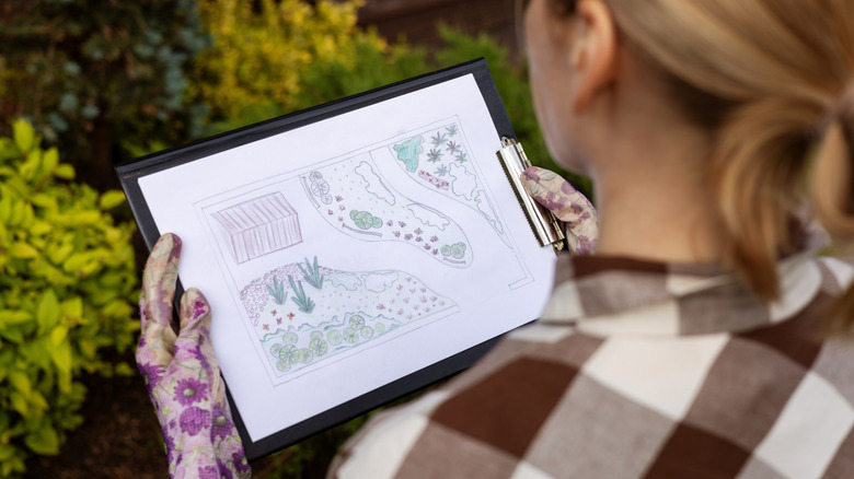 A person looking down at backyard design plans on a clipboard