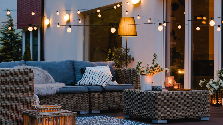 A deck with a couch and string lights, a free-standing lamp, and candles