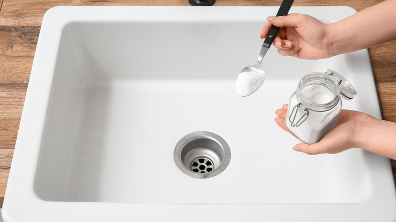 Hand sprinkling baking soda into a white sink