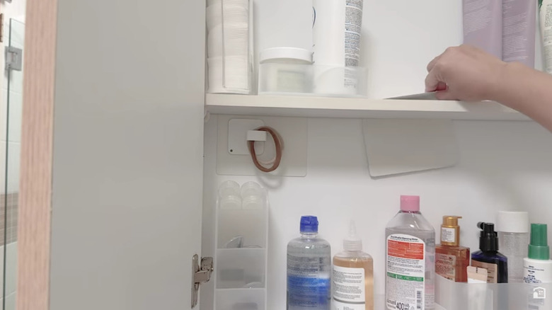 Woman sliding L-shaped bookend behind shelf in a medicine cabinet.