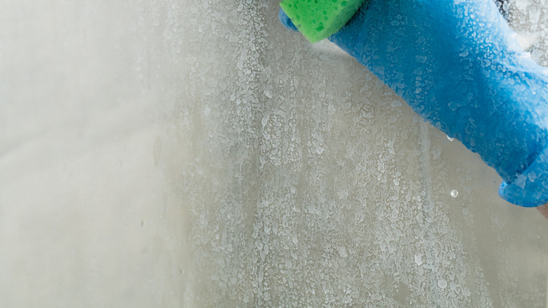 Close up of person wiping shower door with green sponge