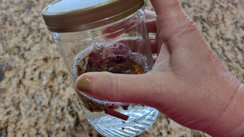 A hand shakes a jar of liquid containing cinnamon sticks.