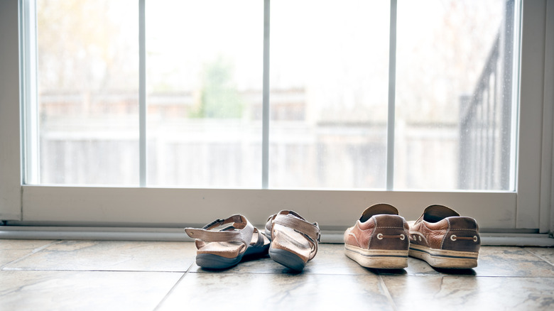 Two pairs of shoes, brown sandals and sneakers, lined up in front of a glass door