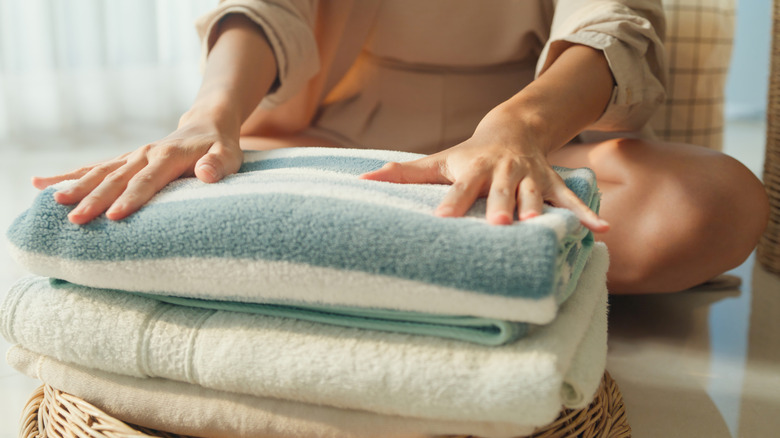 A person sitting cross-legged places their hands on a stack of folded towels.