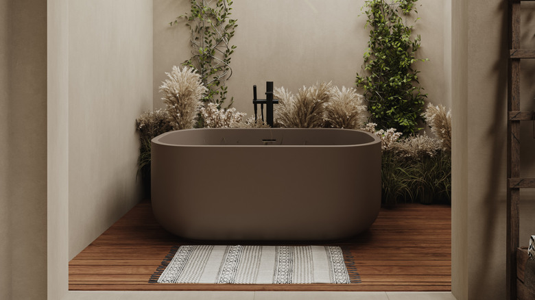 A luxury stand-alone brown tub on a wooden floor with a beautiful bathmat in the front and blant in the background