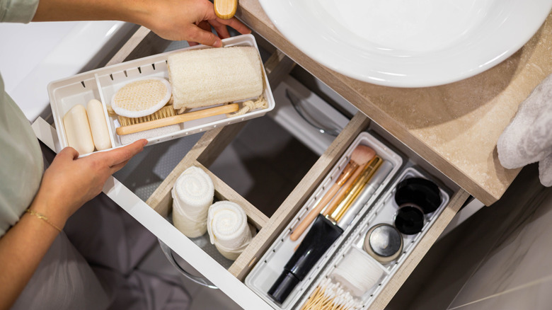 a person is organizing a bathroom drawer with dividers to separate essentials like makeup applicators and hygiene supplies