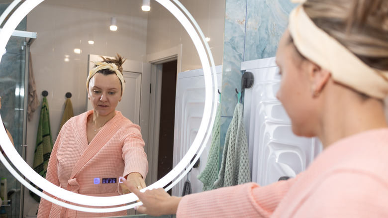 A woman interacting with a smart mirror in a bathroom setting