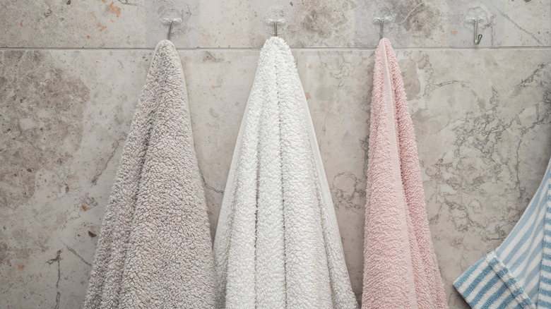 Three towels hanging from adhesive hooks in a bathroom
