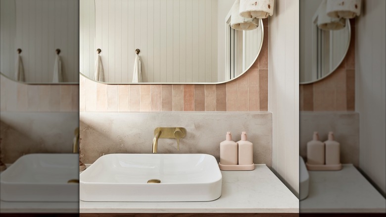 Bathroom vanity with brass faucets and light pink vertical subway tiles.