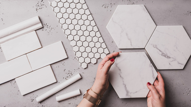 Hands holding hexagonal tile while other tiles and trims are laid out on table.