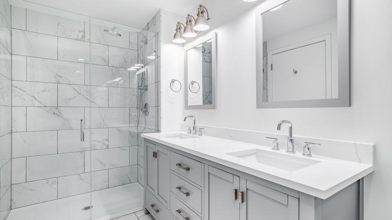 A grey tiled bathroom with multiple chrome fixtures and fittings with a grey vanity u