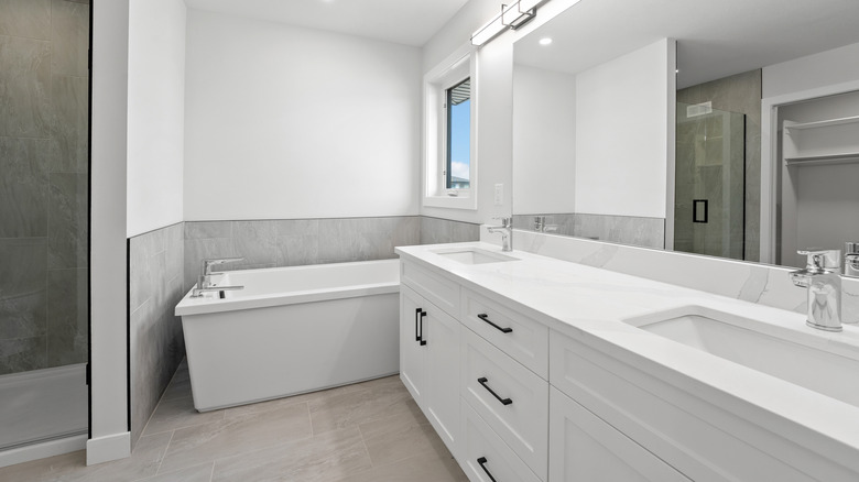 A stark white bathtub, white walls and white countertops and sinks.