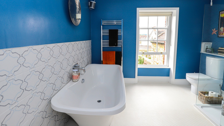 A large bathroom with a big bathtub, glass walled shower and loo with walls painted in a mid-tone cool blue colour.