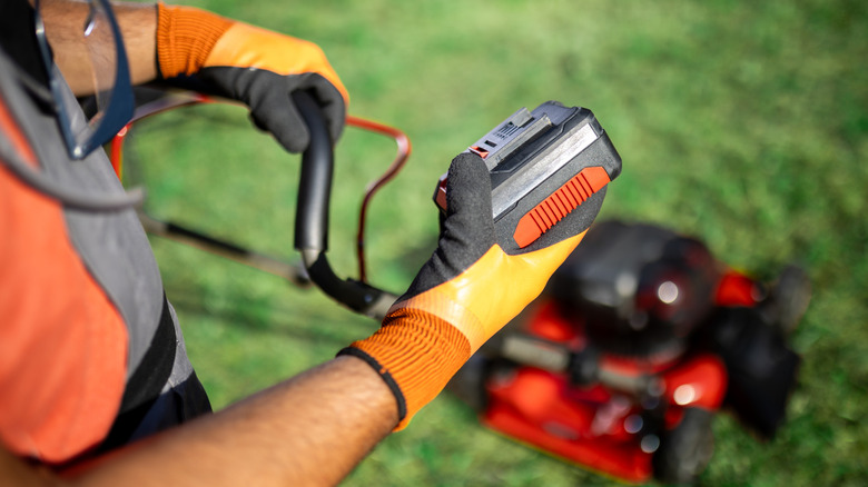 A person holding a battery with a lawn mower.