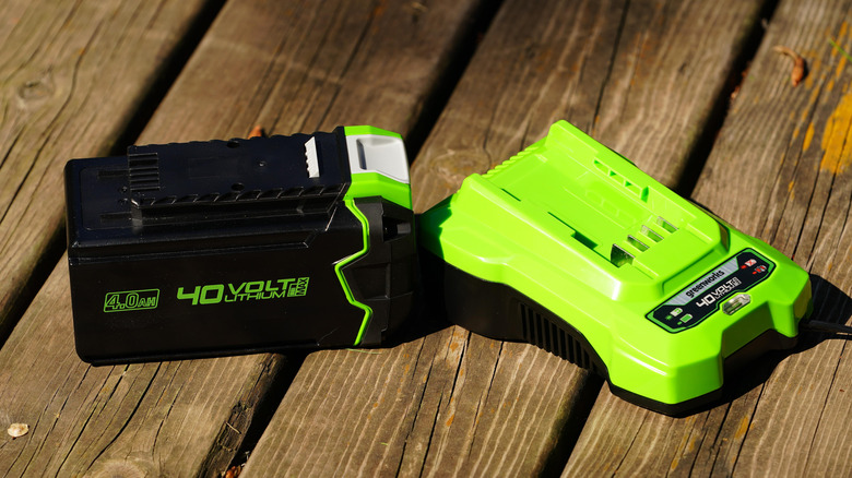 A lawn mower battery and its charger sit on a wooden table.