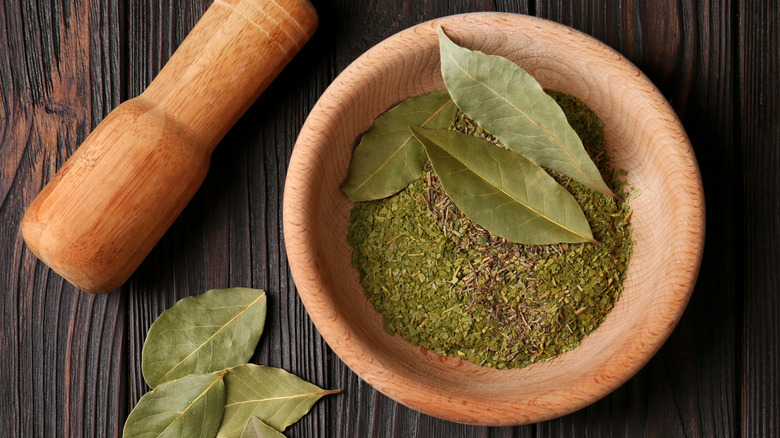 Bay leaves crushed into powder inside a mortar with a pestle nearby on the table