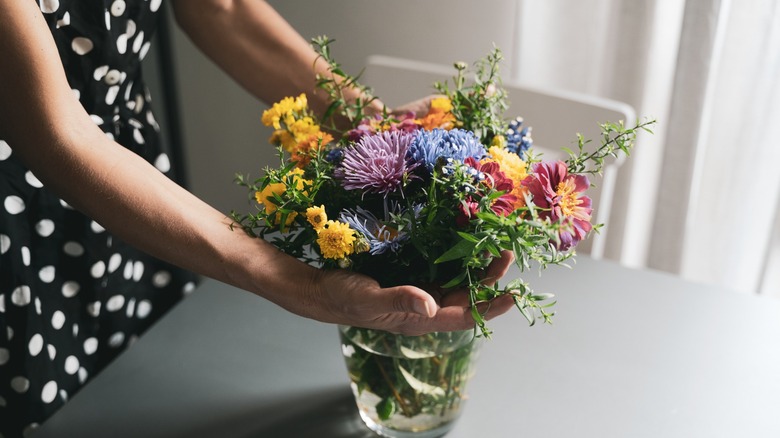 Close up of hands arranging flowers in a glass vase