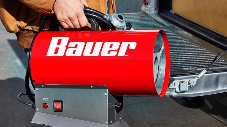 person holding BAUER Forced Air Portable Heater next to truck