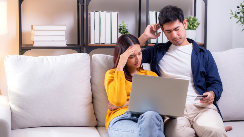 Couple on a couch looking at a laptop with frustration.