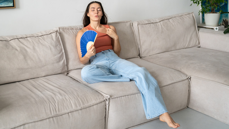 Woman waving paper fan to cool herself in living room