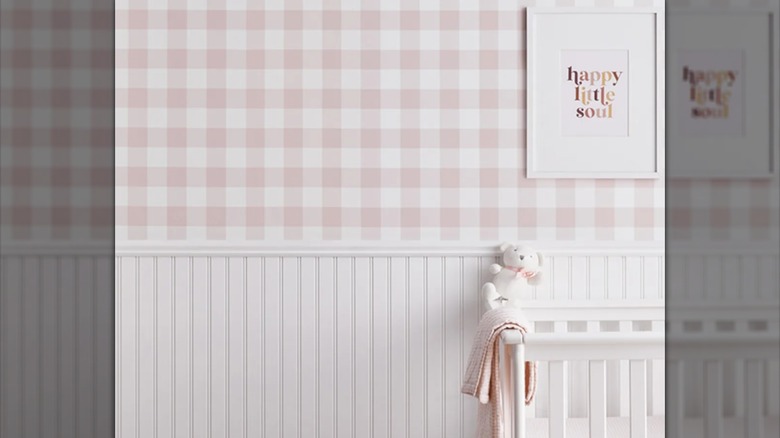 White frame hung on pink gingham wallpaper with crib in front