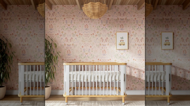 A white and wood crib sits in front of a wall covered in pink floral wallpaper