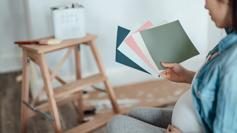 A pregnant woman looks at large paint color samples