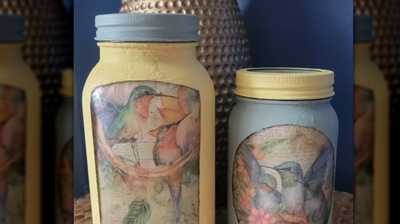 A mirrored image featuring two painted mason jars in blue and yellow with hummingbird pictures inside
