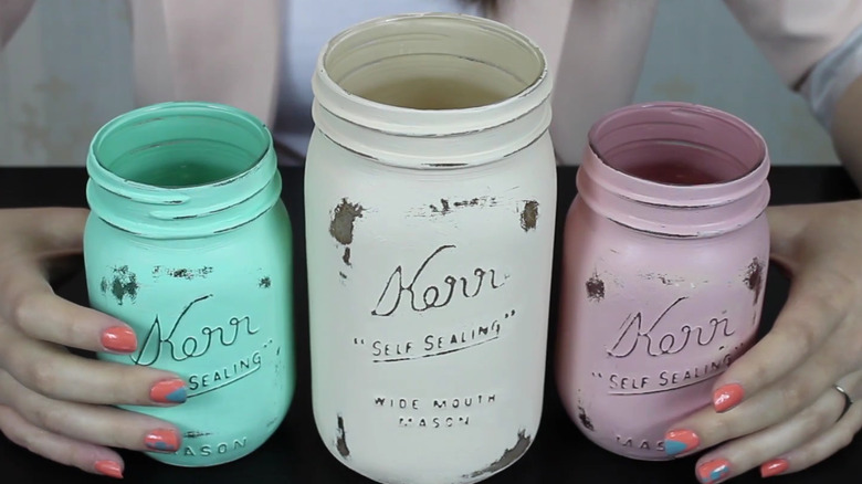 Three mason jars with different colors of distressed chalk paint on them