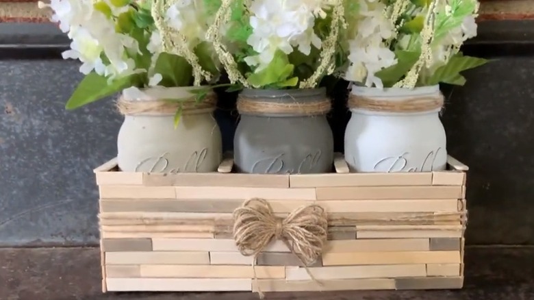 Three chalk painted mason jars holding greenery in a wooden box