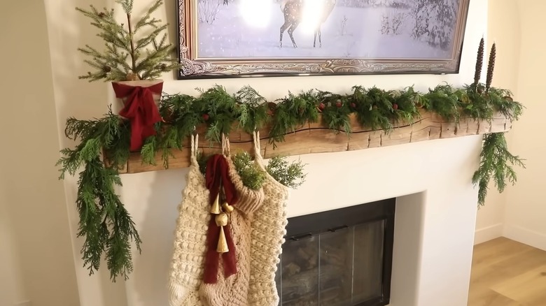 Cedar clippings, dried oranges, and red berries decorate a rough-hewn mantel hung with knit stockings.