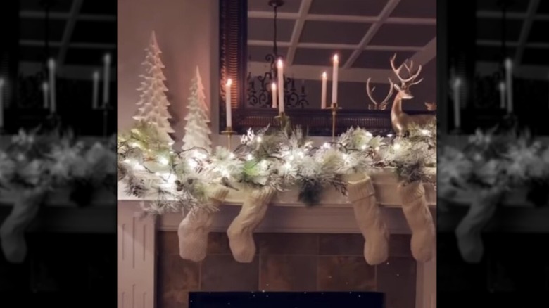 Frosty-looking pine garland with lights, white trees, candles, and deer decorate a mantel.