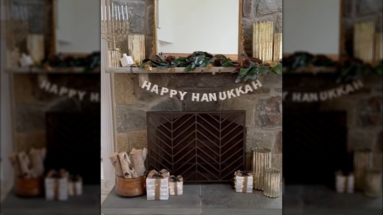 A mantel is decorated with greenery and gold accessories for Hanukkah.