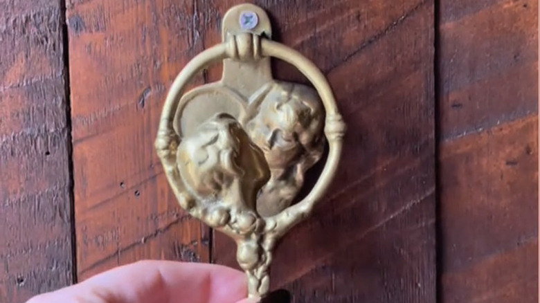 A hand holding a vintage gold door knocker
