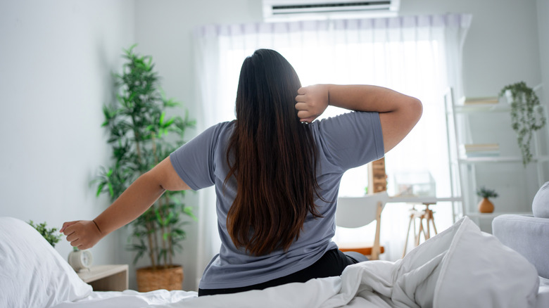 woman wearing pajamas in bedroom stretching in the morning after waking up