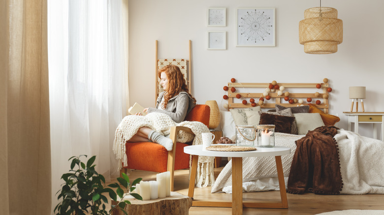 young woman in her bedroom, sitting in a chair reading with blanket