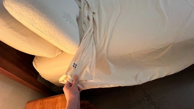 Hand pulling sheet corner on a partially made bed.