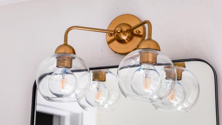 A brass overhead lighting fixture made of glass placed above a bathroom mirror