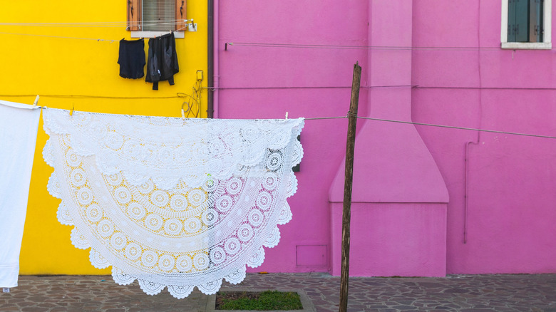 A white crocheted tablecloth is pinned to a line to dry next to pink and yellow walls.