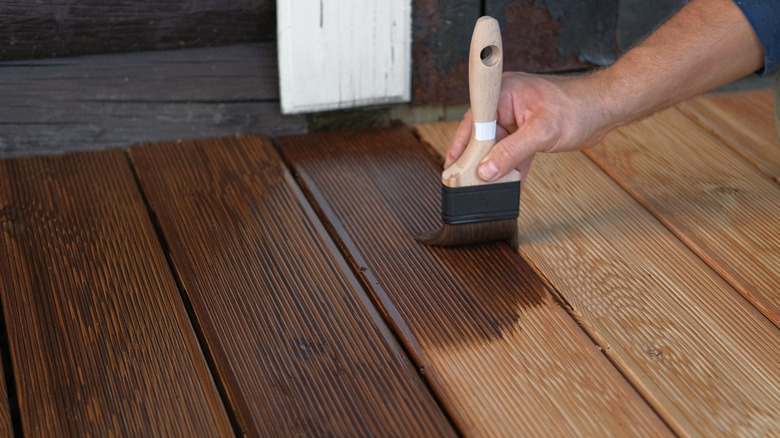 Person's hand applying wood stain to deck