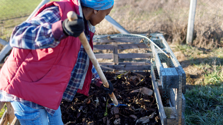 A woman turns a compost pile with a pitch fork