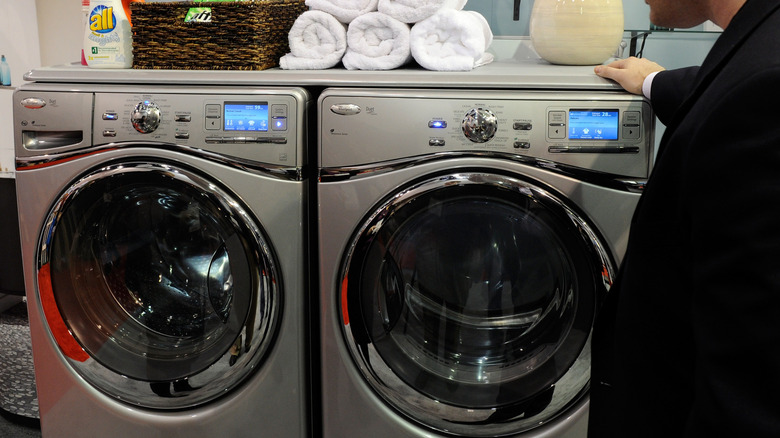 Man standing beside a Whirlpool washer and dryer combo in a laundry room