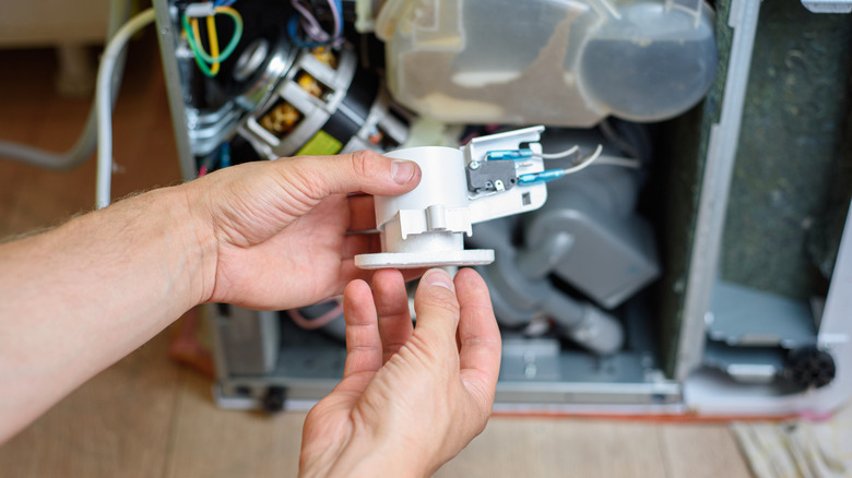 Technician adding a new replacement part to a broken dishwasher